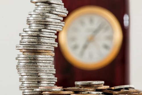 stack of coins in foreground with clock in background to symbolize savings