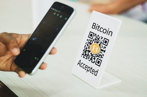 Close up of hands by using mobile phone Scaning Bitcoin QR code for digital contact less payment after shopping using Bitcoin cryptocurrency - concept of technology, safety and privacy